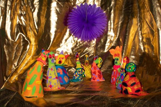 各种各样的陶瓷娃娃排列在一块金色的布上，上面有一朵紫色的花.