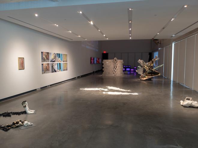Art gallery with various sculptures on the floor and photographs along the right wall. 